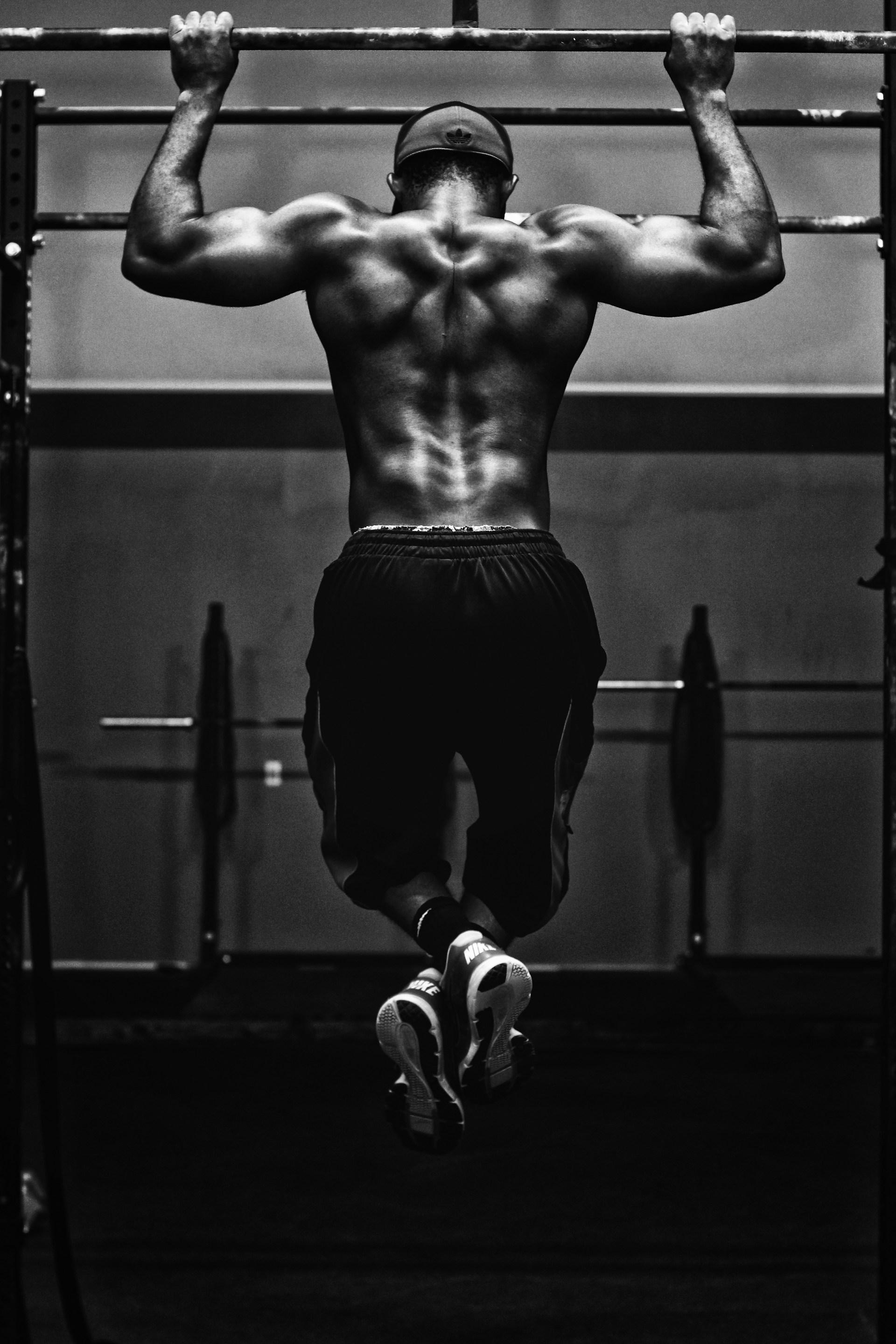 An athlete performing a pull-up, photographed from behind in black and white