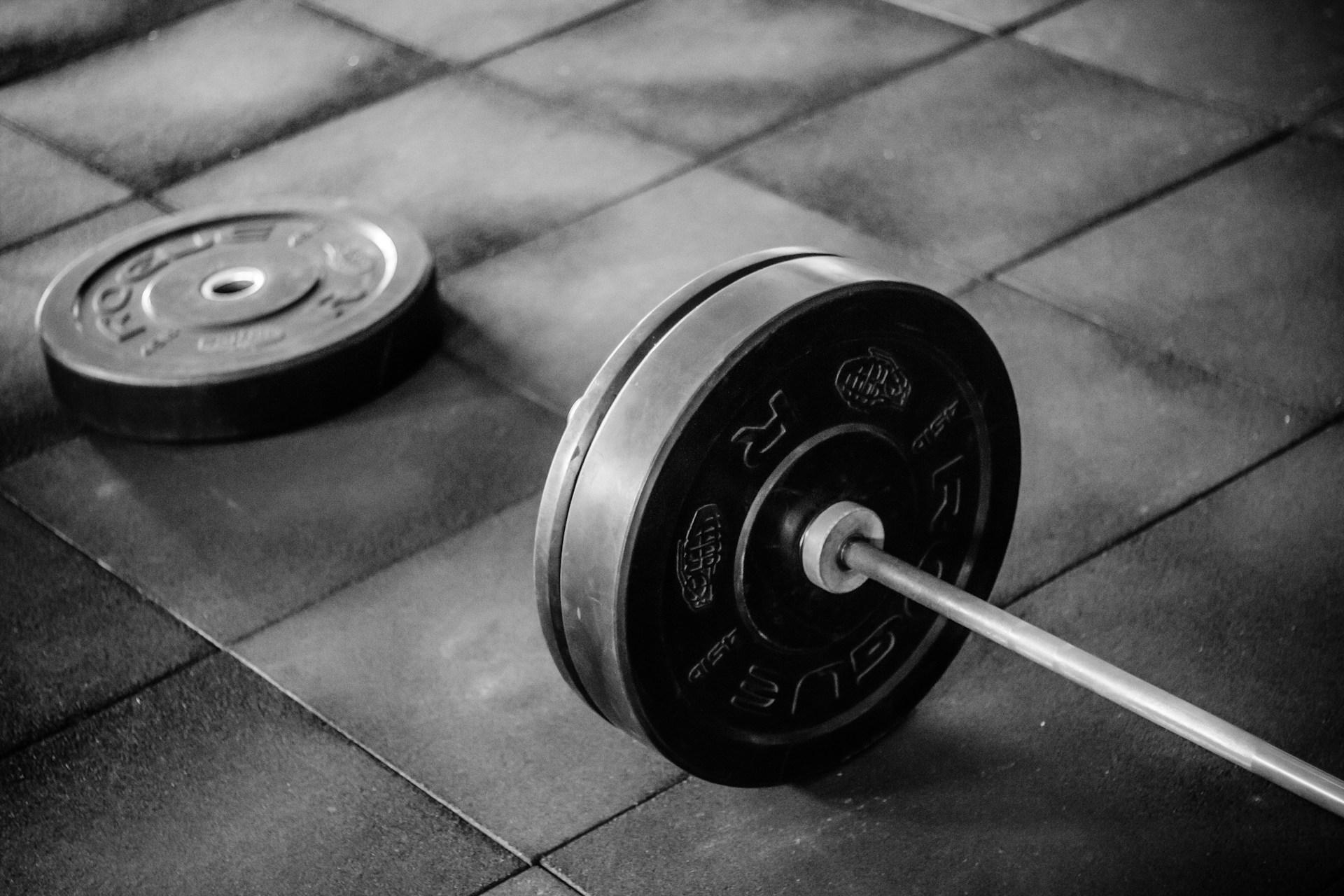 A loaded barbell and bumper plate on a rubber gym floor, in black and white
