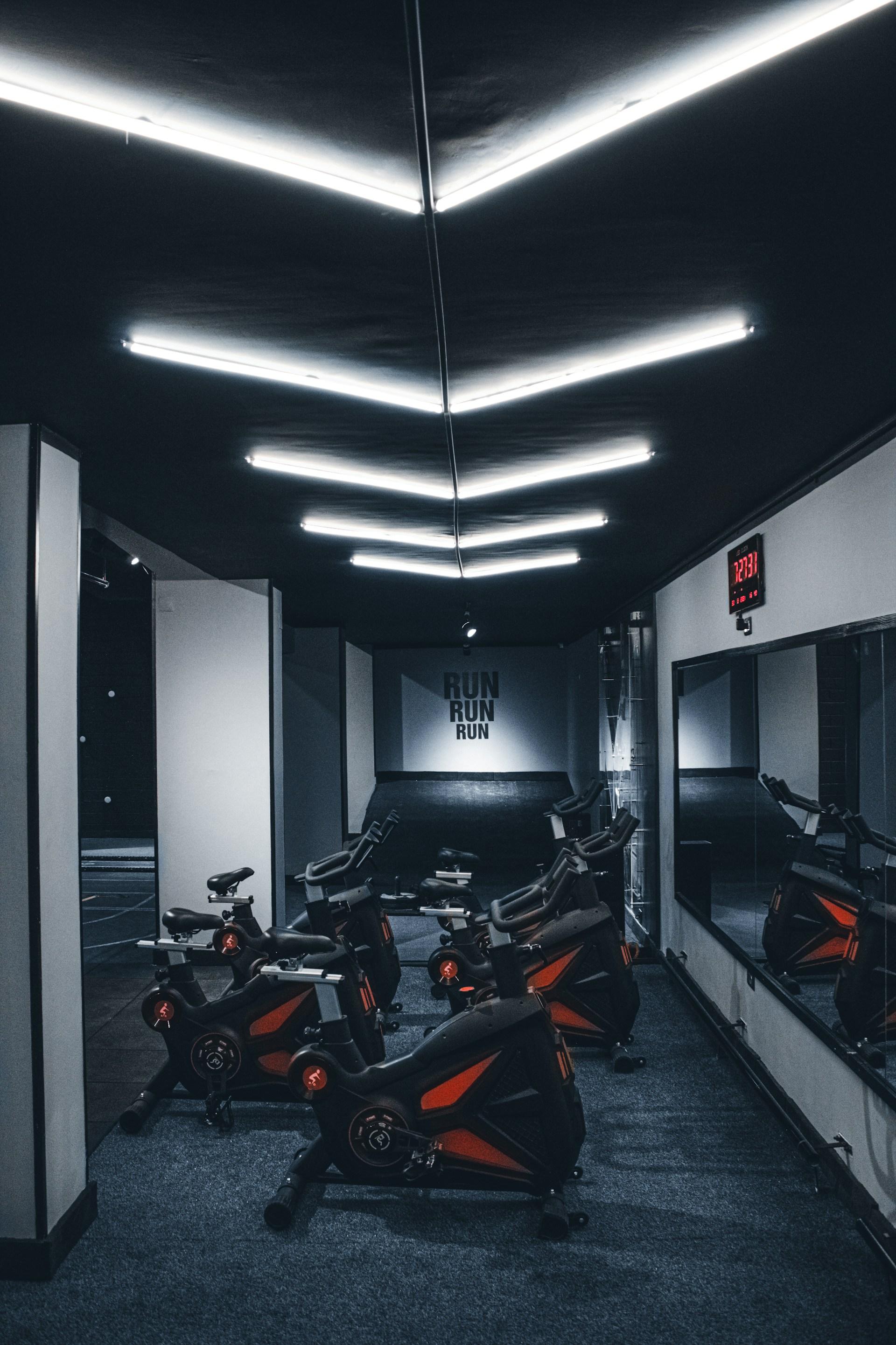 A row of indoor exercise bikes under strip lighting