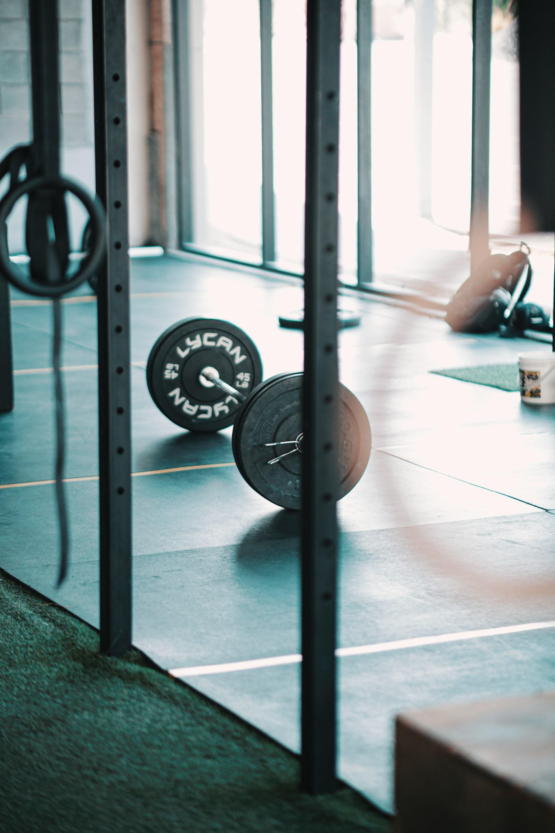 A barbell on the floor beside a rig with gymnastic rings