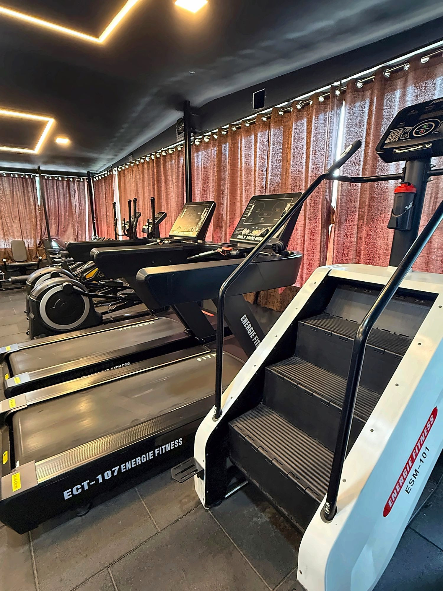 A row of treadmills, ellipticals and a stair climber in the EMPIRE GYM cardio area
