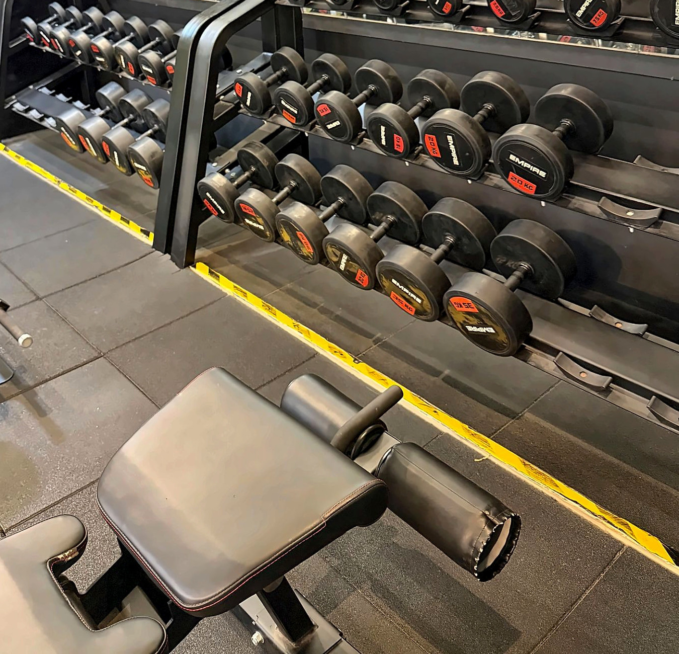 Racks of EMPIRE-branded dumbbells beside a bench on rubber flooring