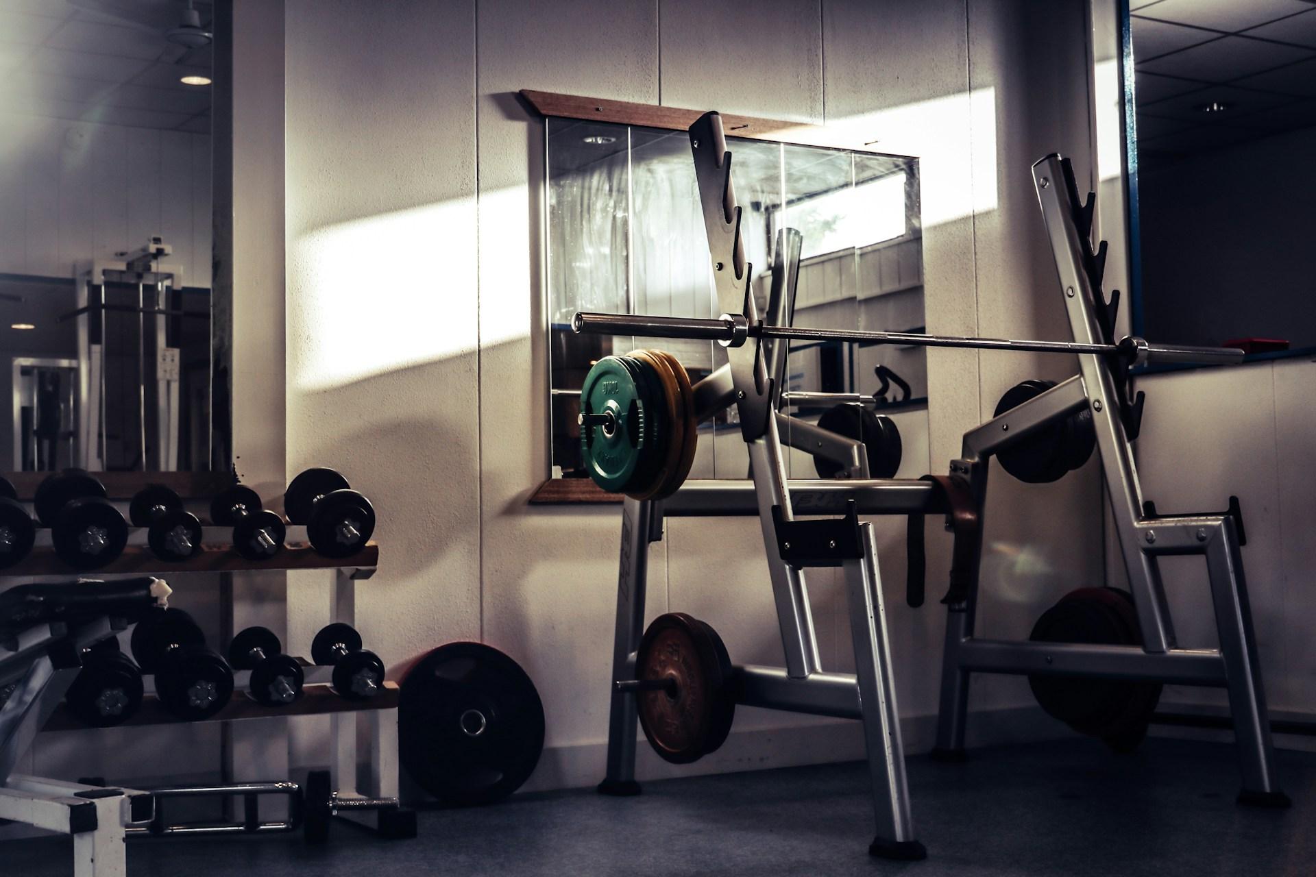 A barbell resting on a squat rack in a sunlit gym