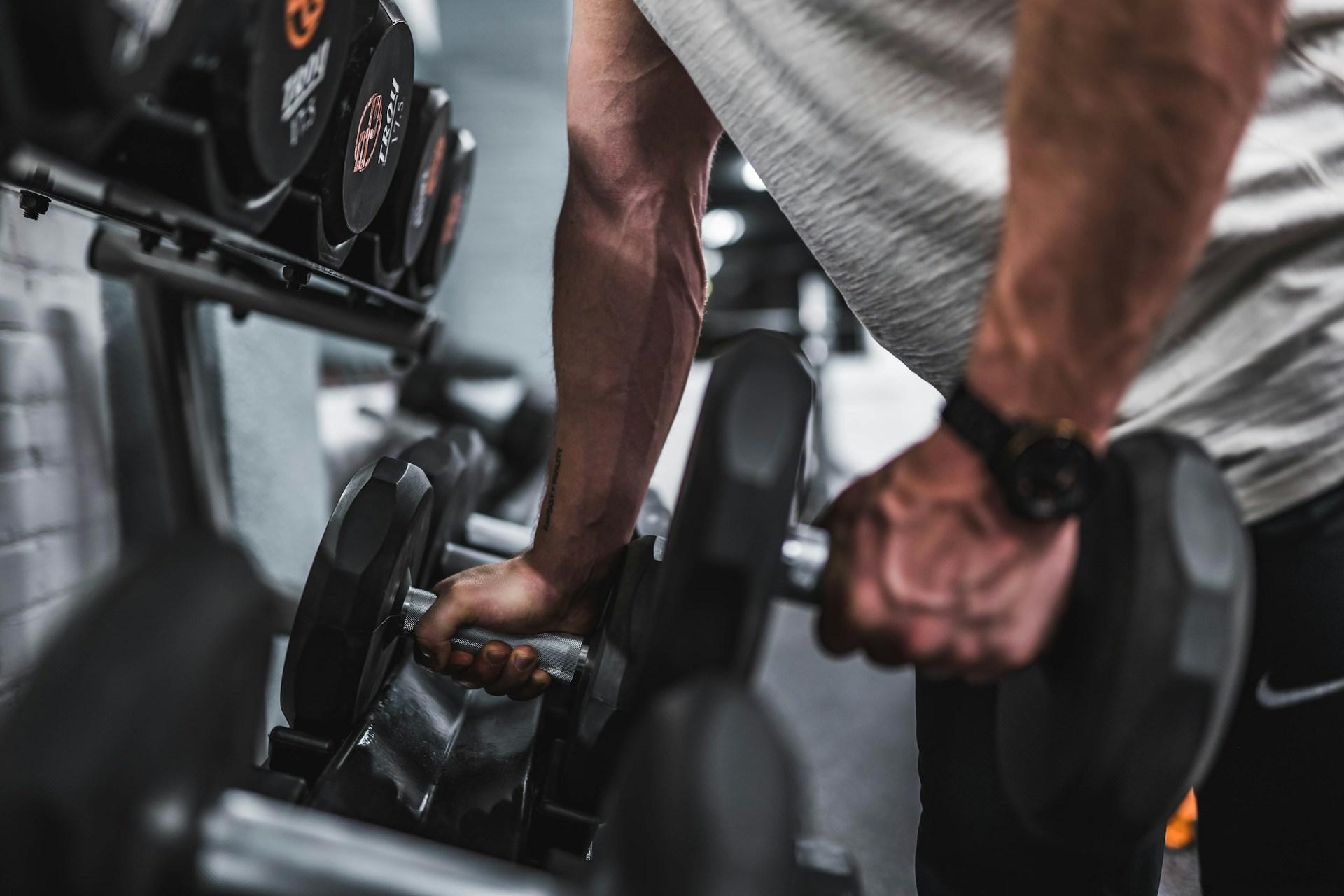 A person in a grey t-shirt lifting a dumbbell from a rack